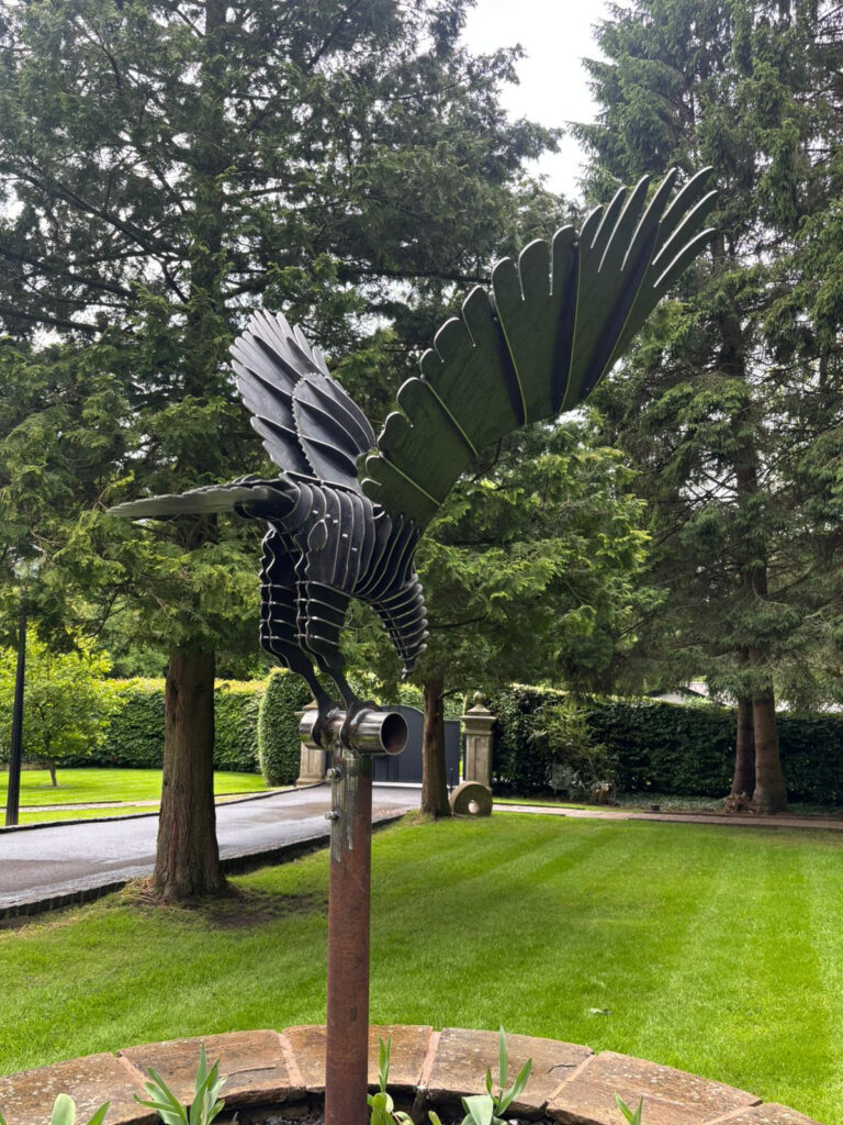 a metal sculpture of a bird in a garden