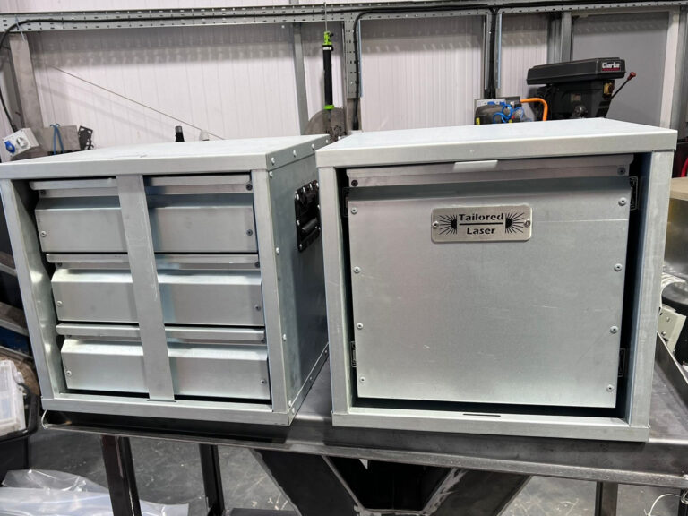 Two custom metal van storage units with drawers and Tailored Laser branded panel on a workshop bench
