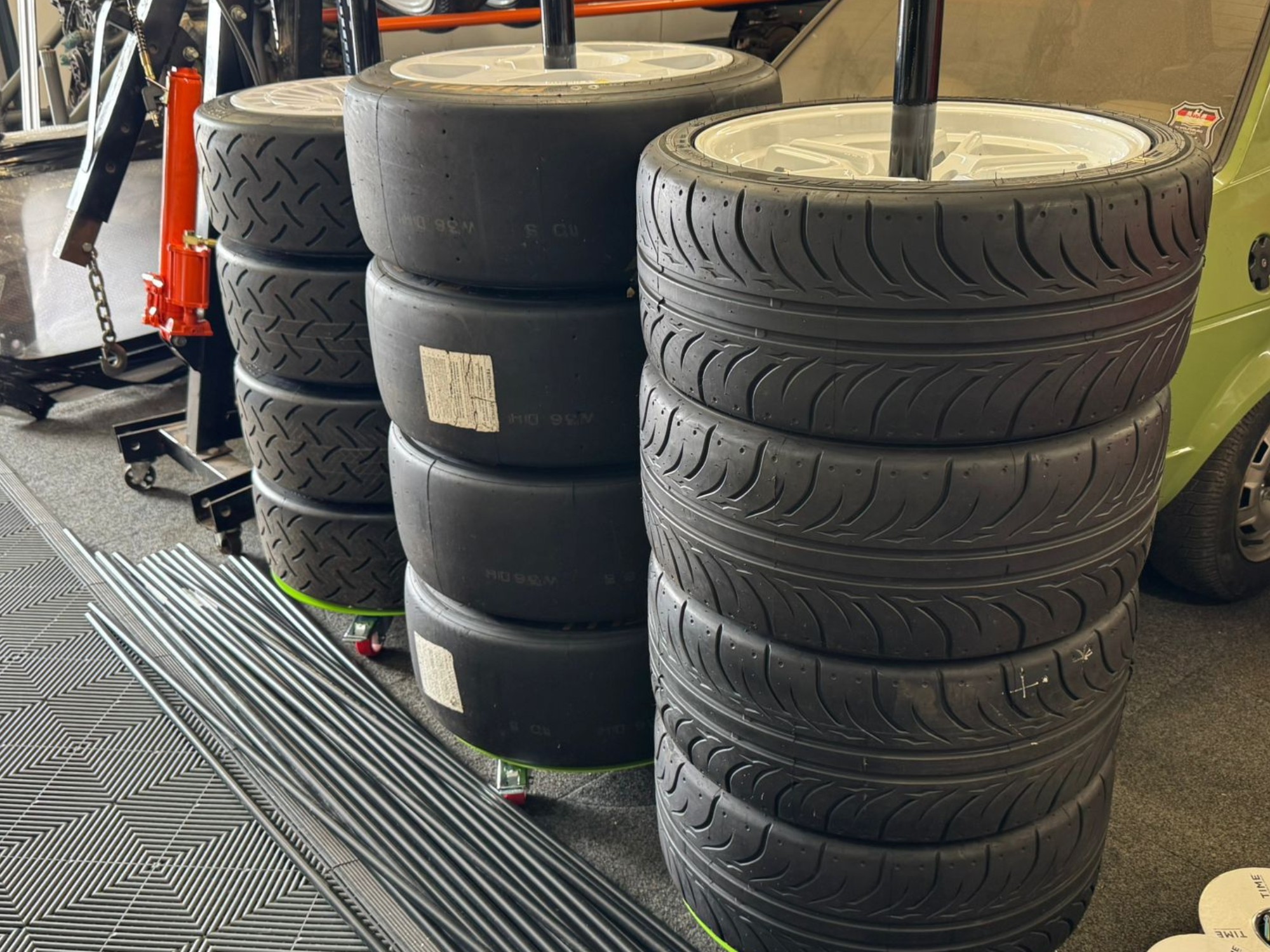 Stacks of racing tyres with alloy wheels in a motorsport workshop with tools and equipment