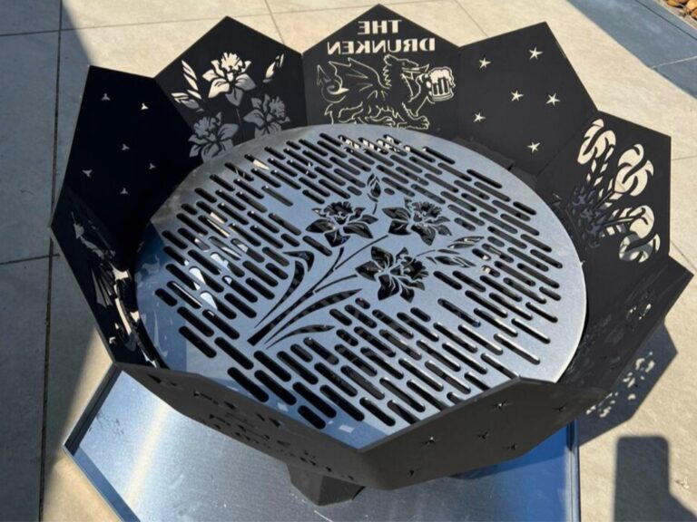 Decorative laser‑cut steel fire pit with floral patterns and griffin artwork casting shadows on outdoor tiles