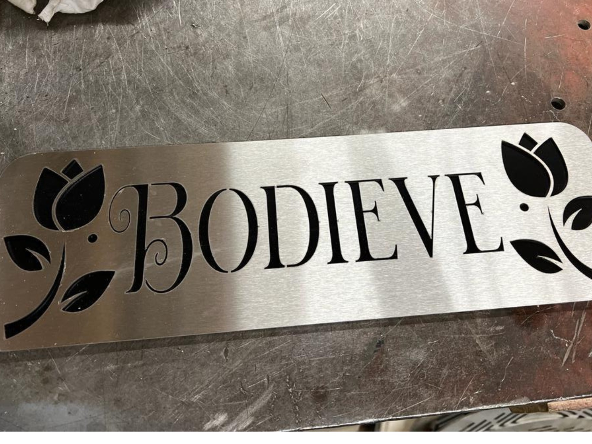 Laser‑cut metal sign with BODIEVE text and floral cut‑out designs
