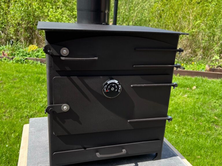 “Black outdoor wood‑fired oven with chimney, temperature gauge, and steel door in a garden setting