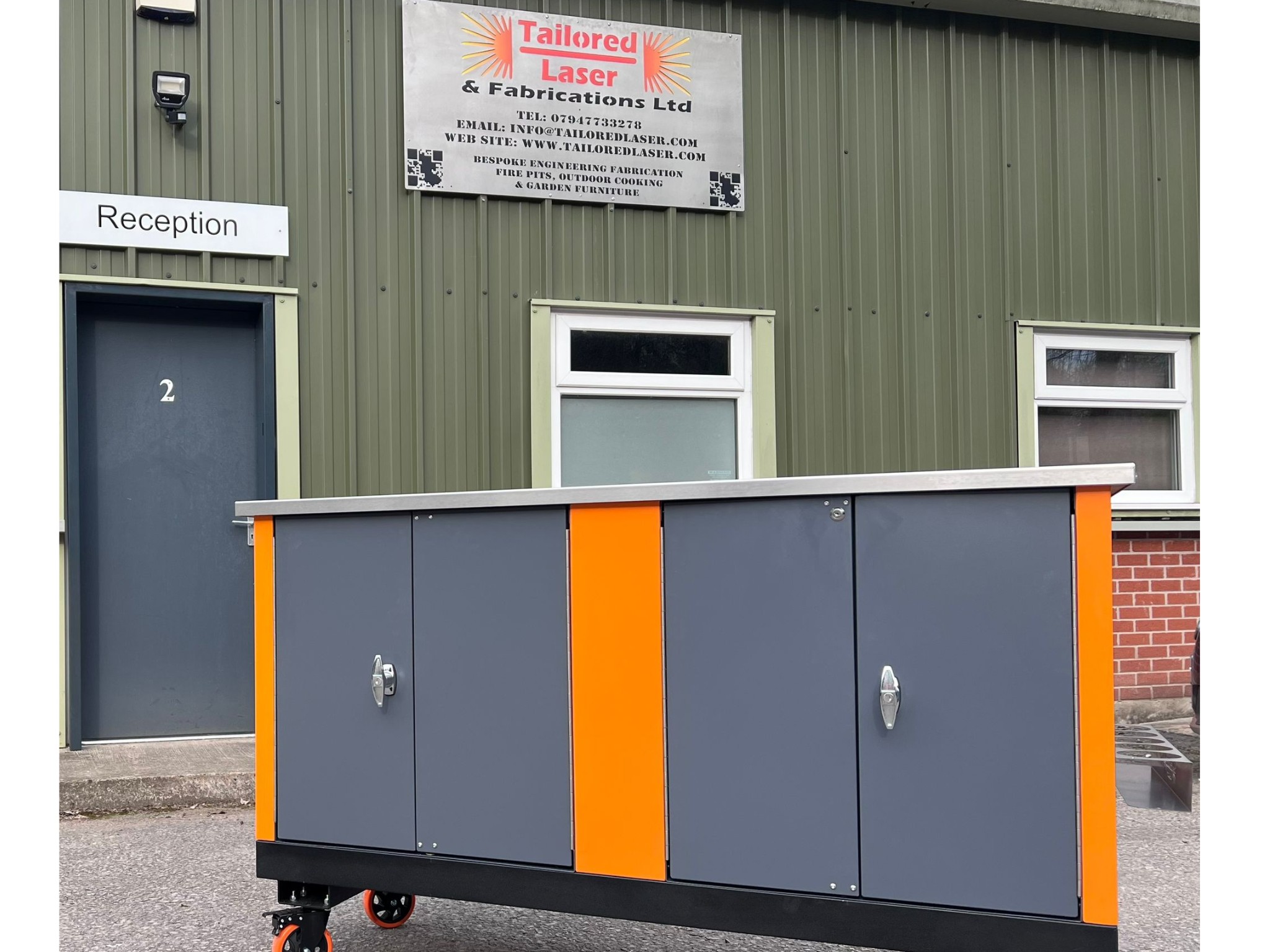 Grey and orange workshop cabinet with stainless steel top outside Tailored Laser workshop