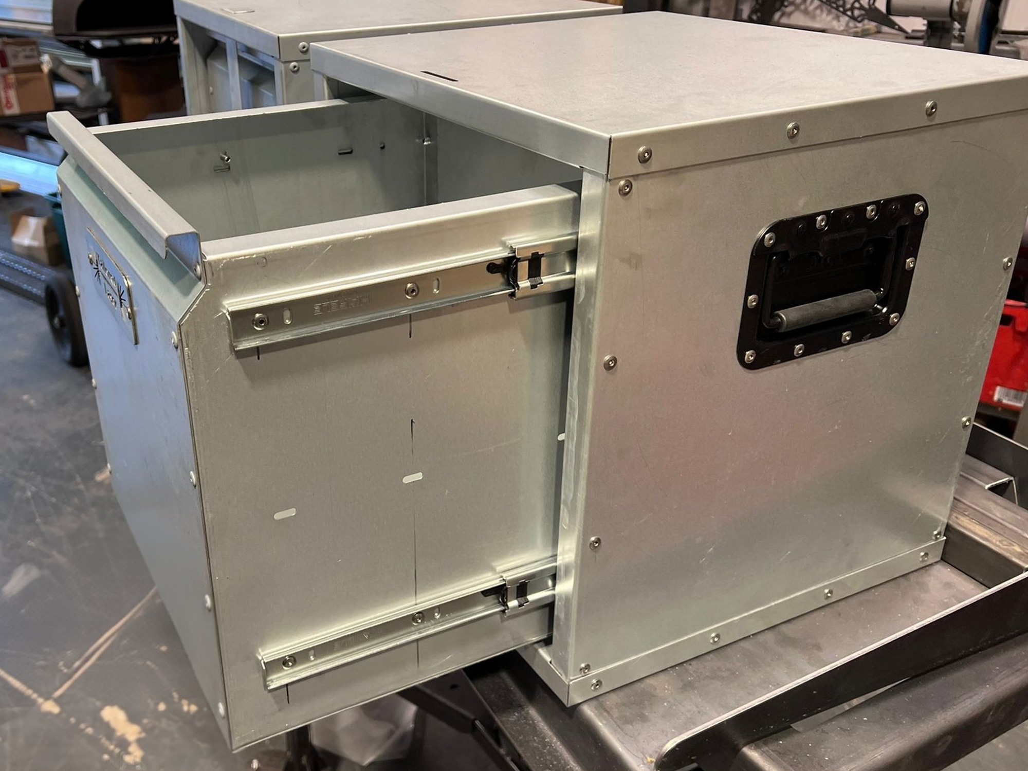 Metal van storage drawer unit with sliding drawer and reinforced corners on a workshop bench