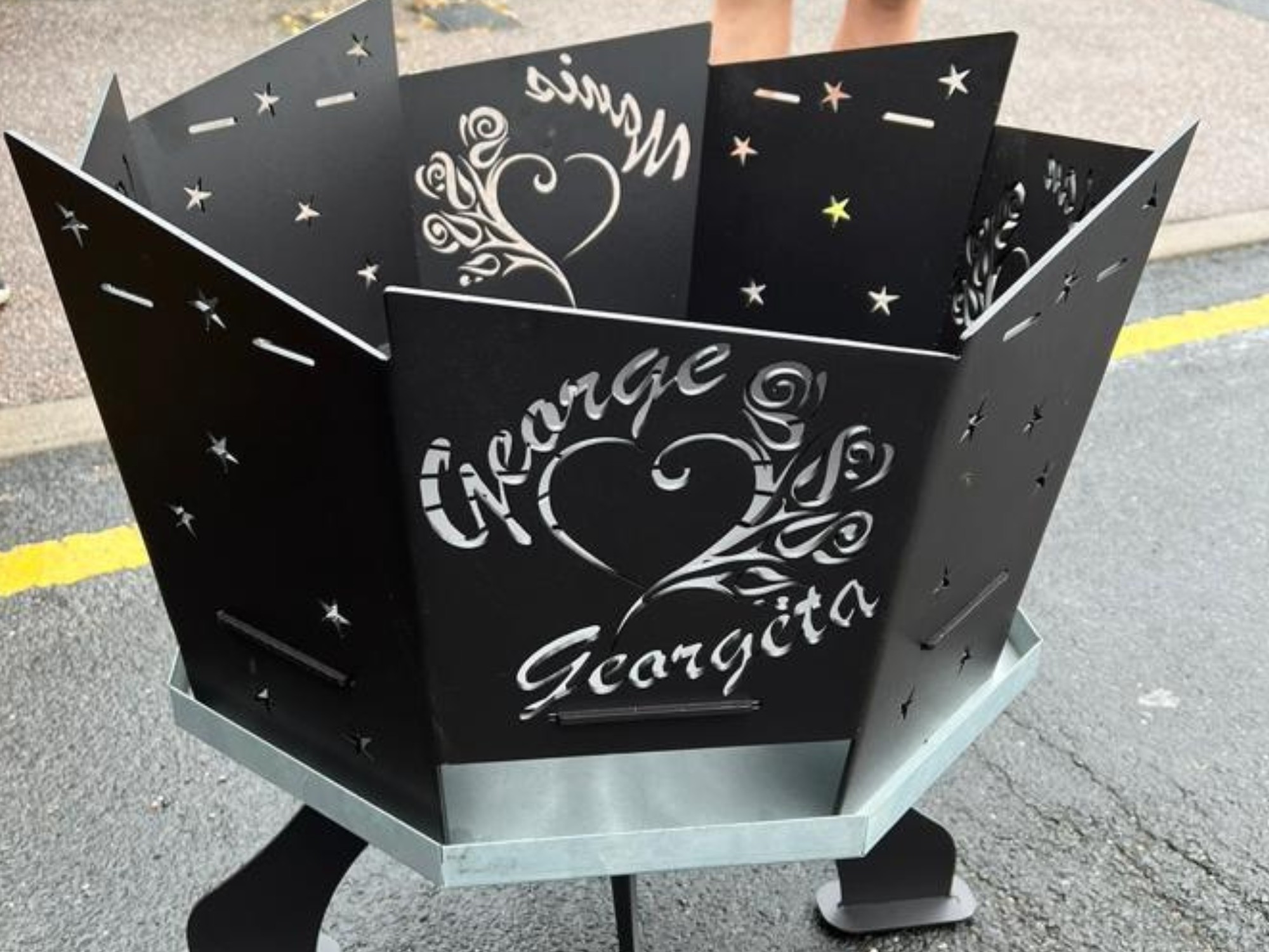 Personalised black steel fire pit with laser‑cut star patterns and George ❤️ Georgeta design on a metal stand.