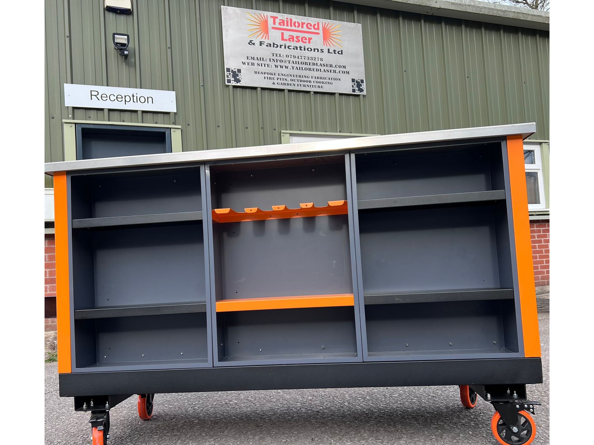 Large grey and orange workshop unit with stainless steel top and open shelves outside Tailored Laser